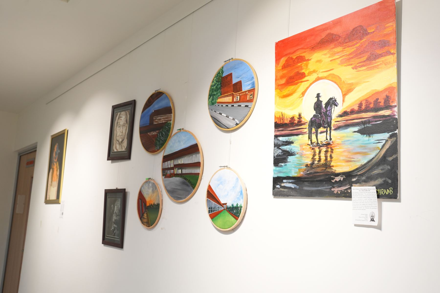 Student paintings, including campus scenes in embroidery hoops, on the TSLAS gallery wall